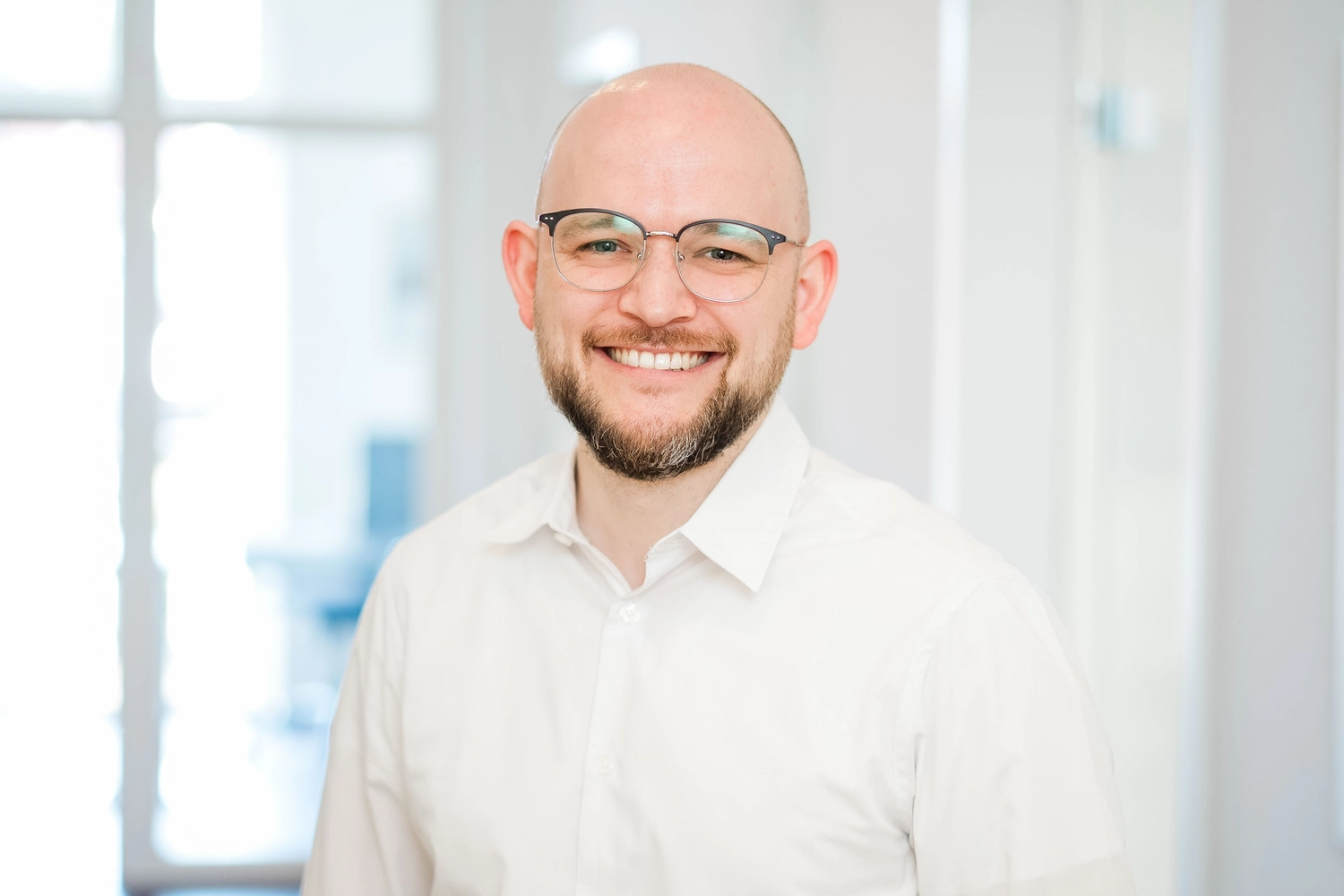 Lächelnder Mann mit Brille und Bart im hellen Büro, Business-Porträt